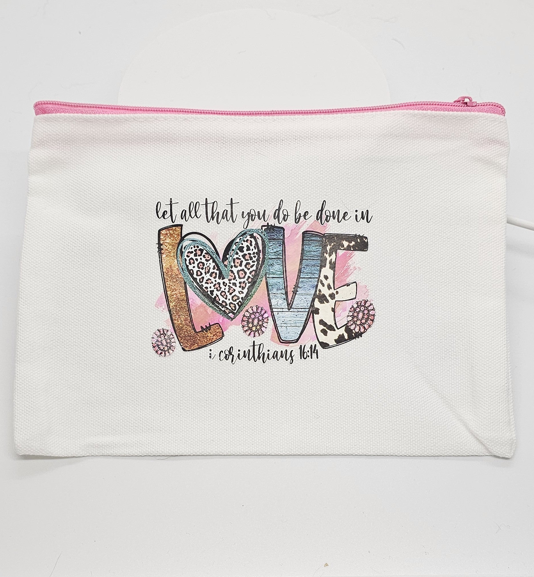 White pouch with 'let all that you do be done in love' text and colorful letters on a white background