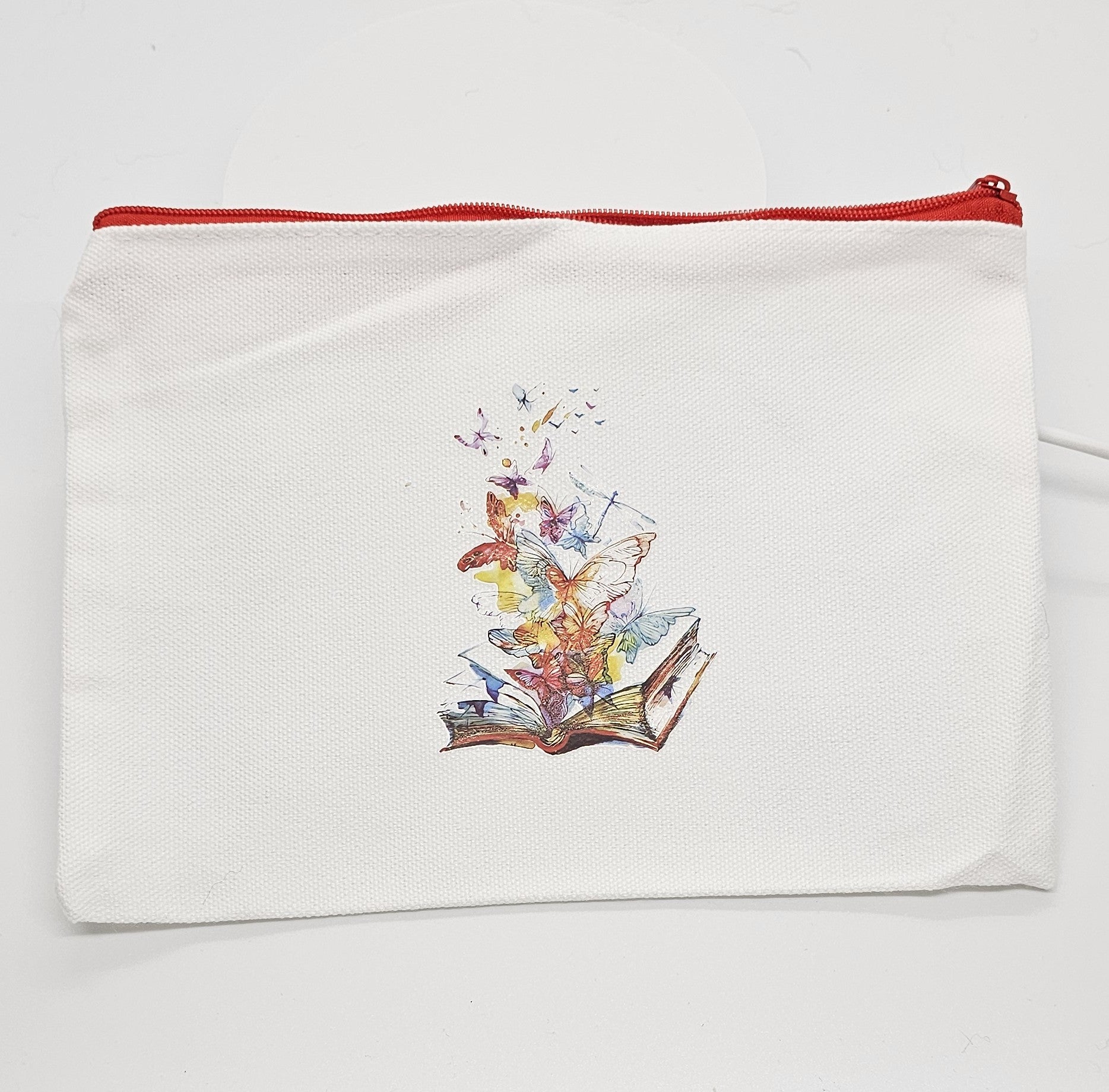 White pouch with a colorful design of an open book releasing butterflies on a white background